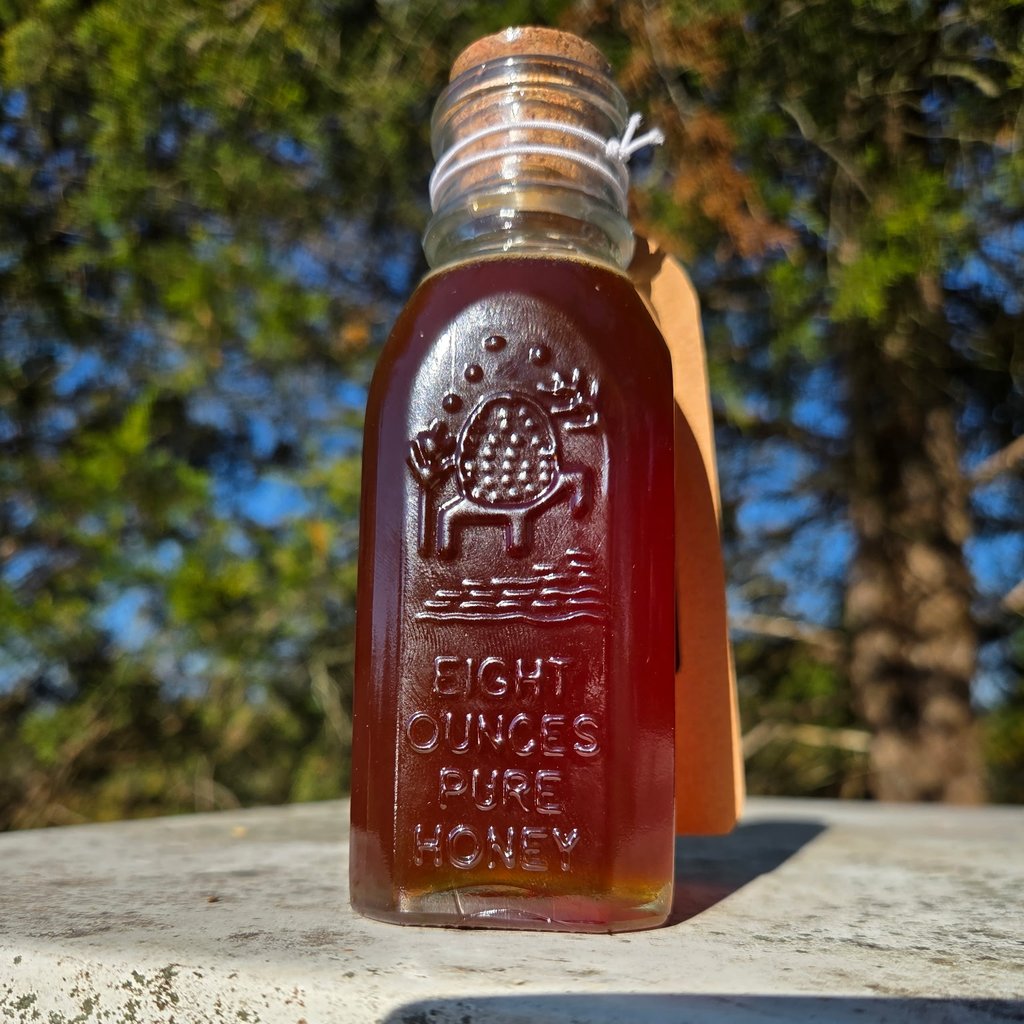 Eight-ounce glass bottle of dark amber raw honey with a cork stopper, embossed Eight Ounces Pure Honey